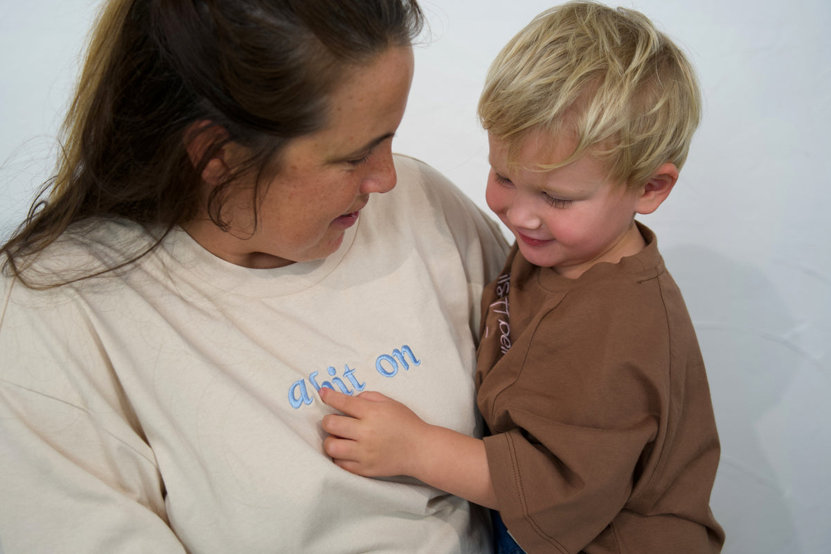 Close-up of an adult wearing the Oat Momenta women’s tee with a child in the Mud kids tee.
