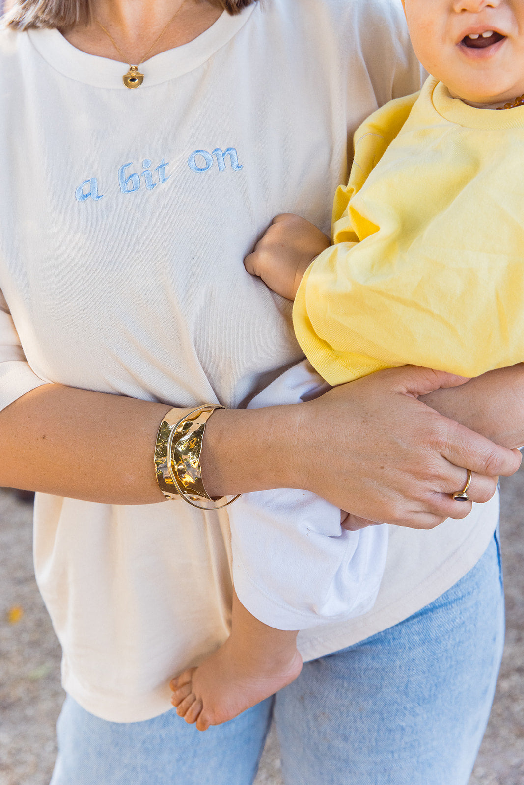 Close-up of a Momenta Oat tee with light-blue embroidery, beside a child in a yellow tee.