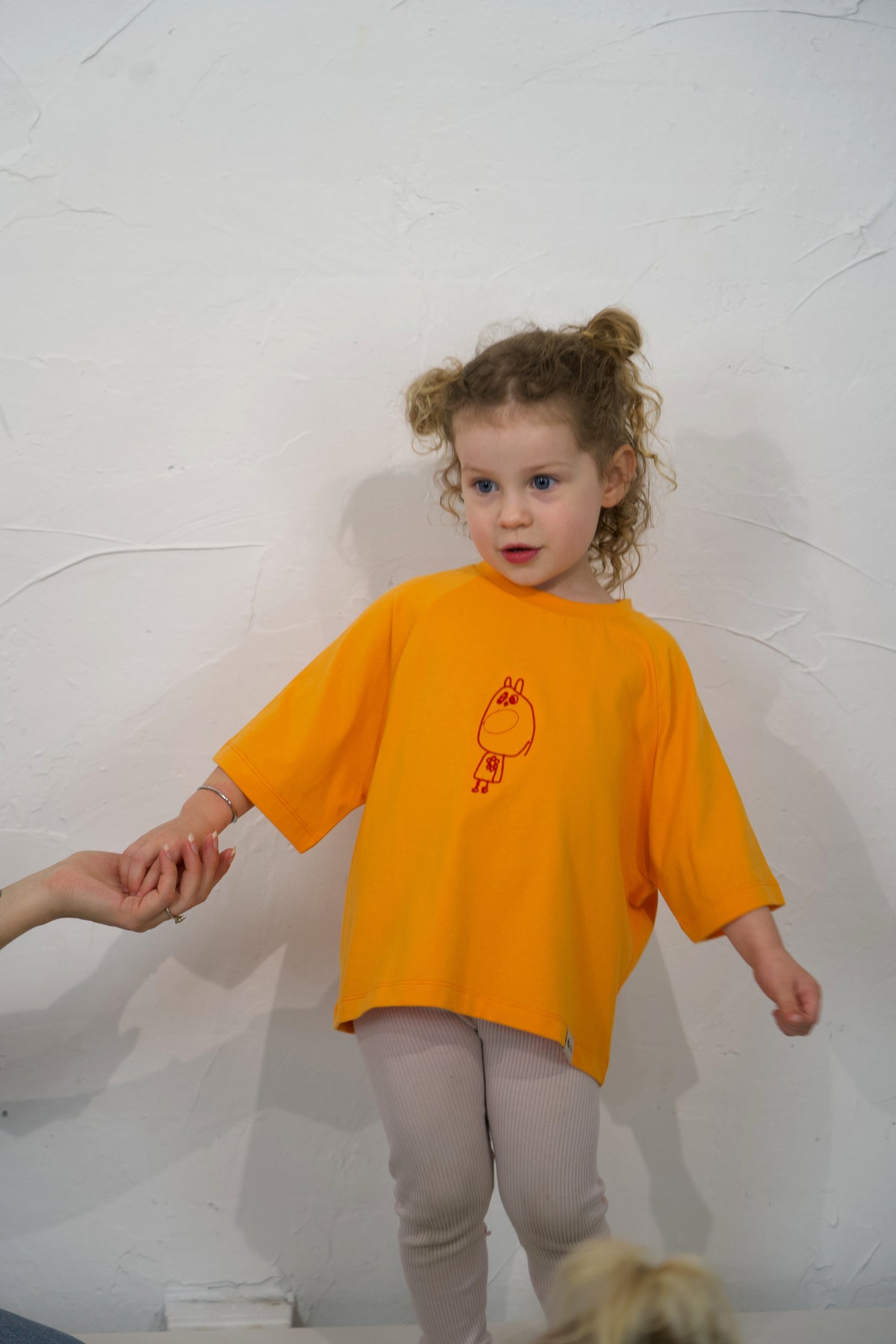 Child wearing the orange Mandarin Momenta kids tee with an embroidered drawing.