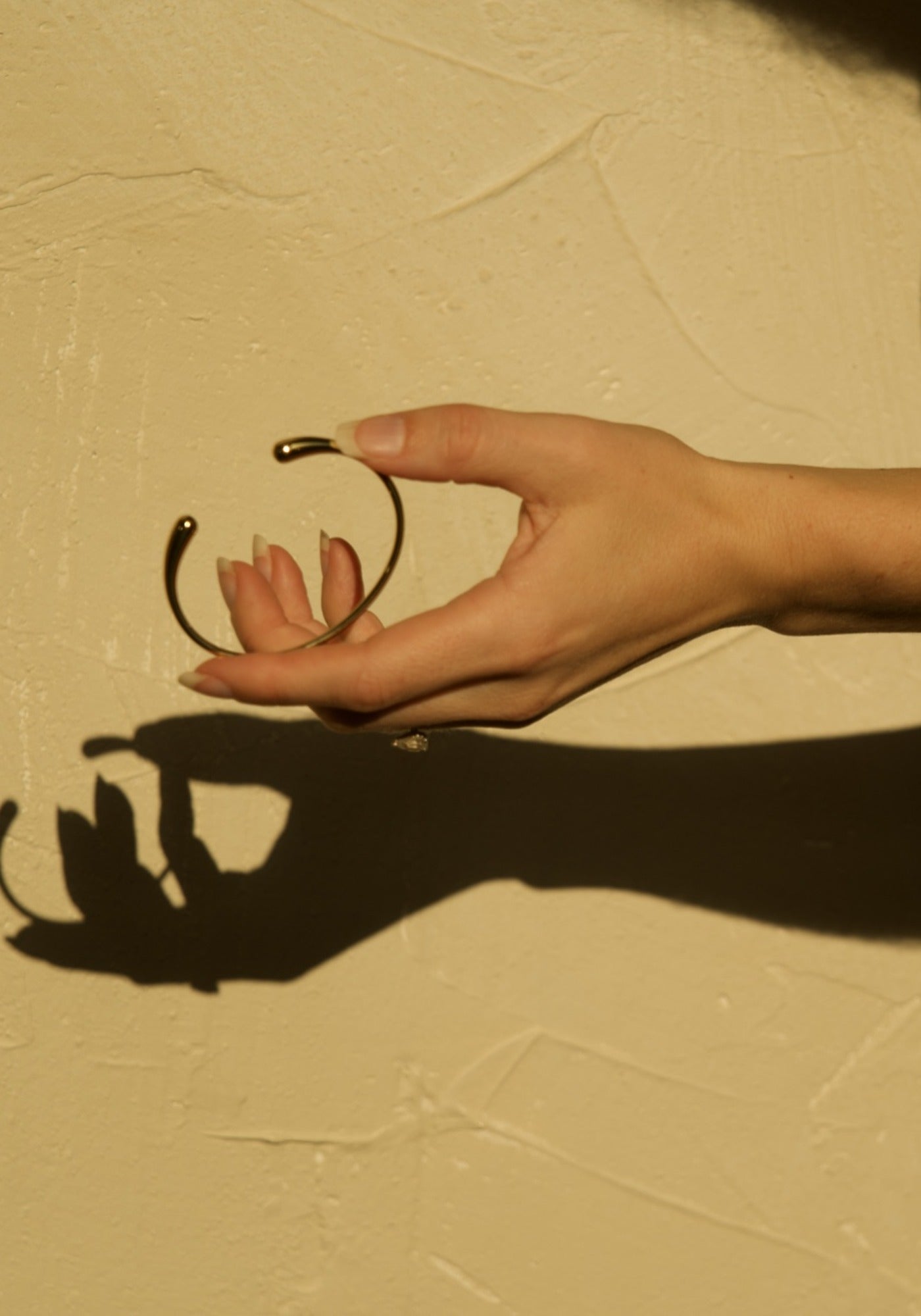 Minimal Bracelet in gold held in the sunlight