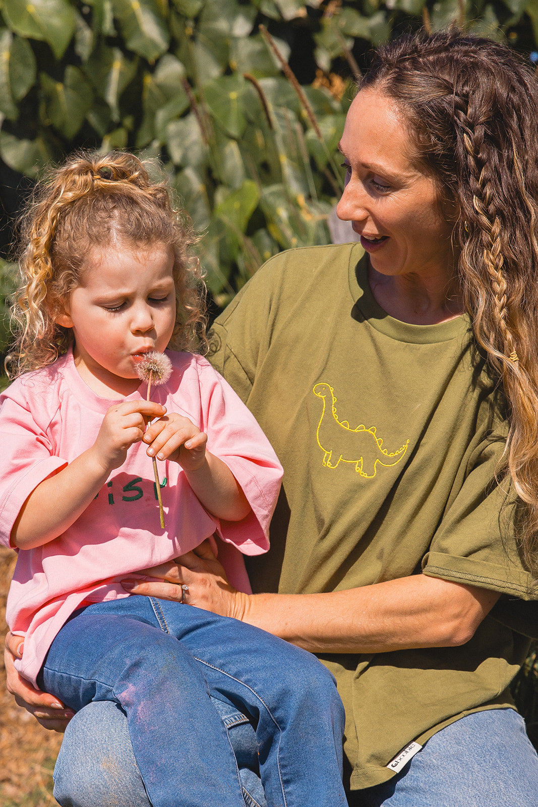 Momenta farm shoot: an adult in an olive tee with yellow dinosaur embroidery holding a child in a pink embroidered tee.