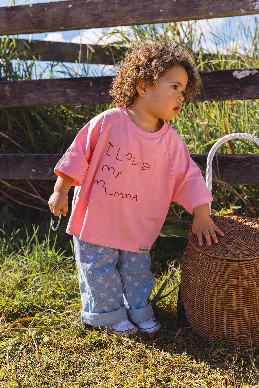 Momenta farm shoot: a child in a pink tee with handwritten I love my mumma embroidery beside a wicker basket.