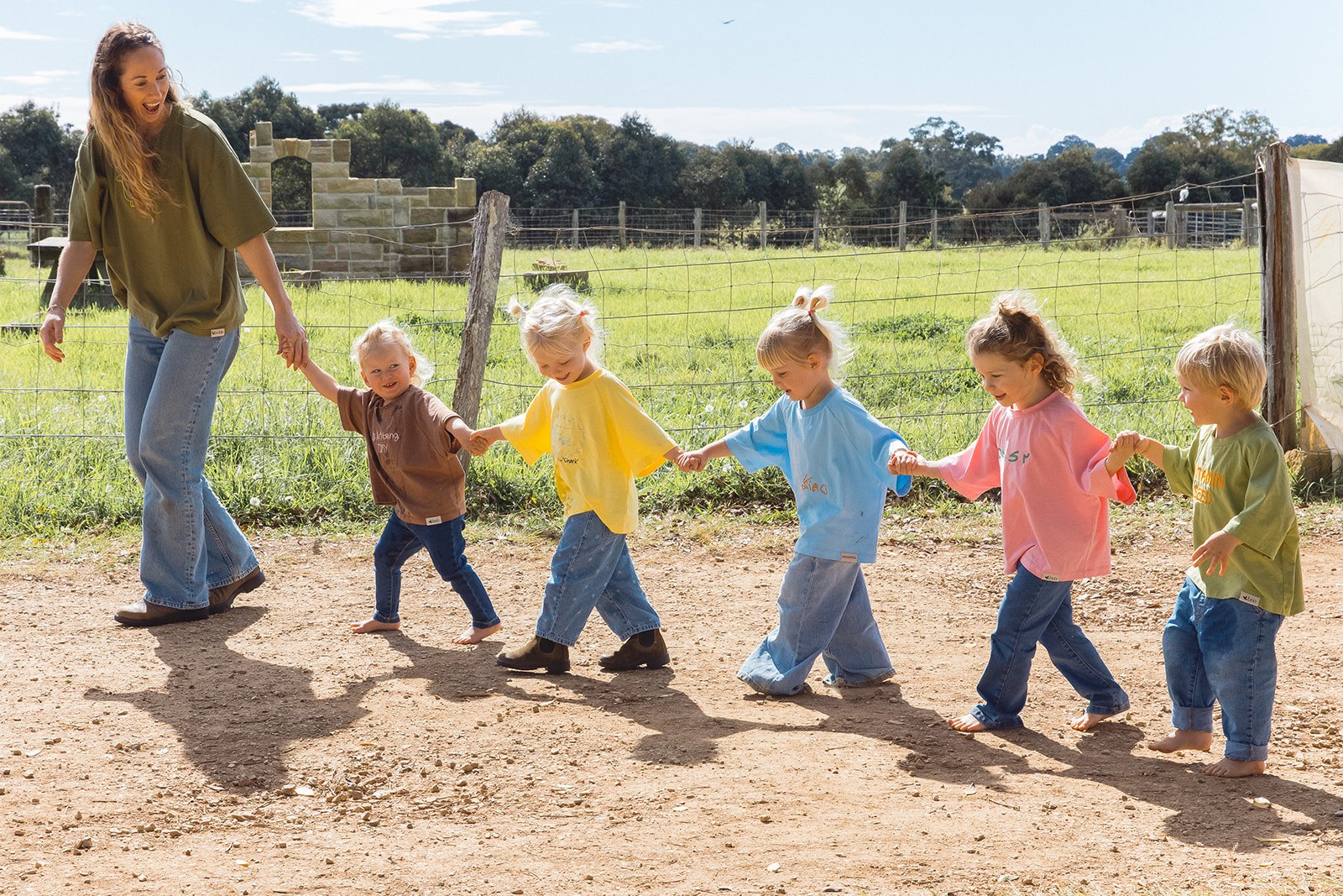 An adult and five children holding hands in colourful embroidered Momenta tees